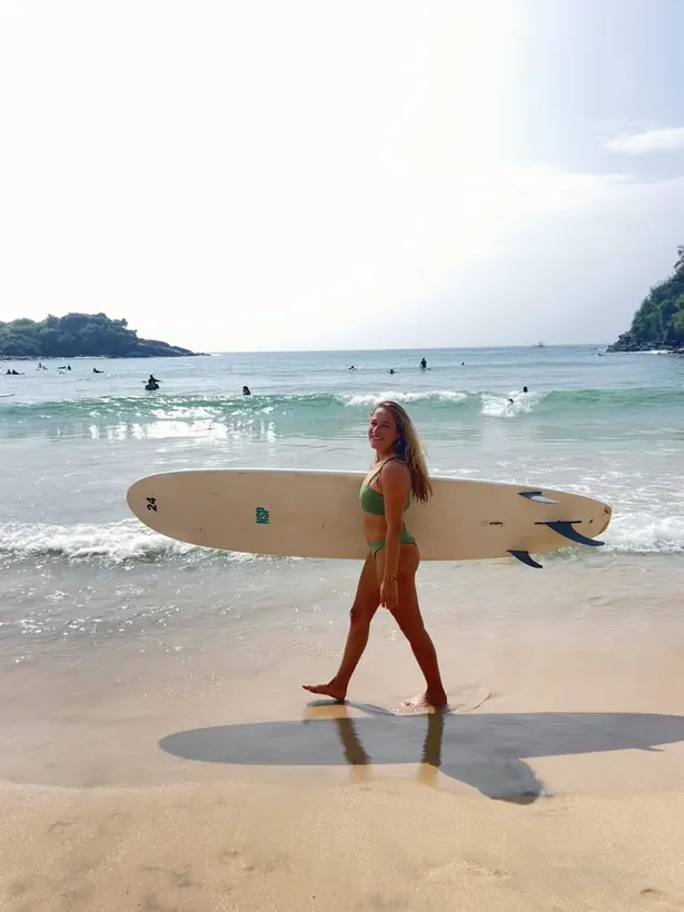 Evelyne walking along the beach with a longboard